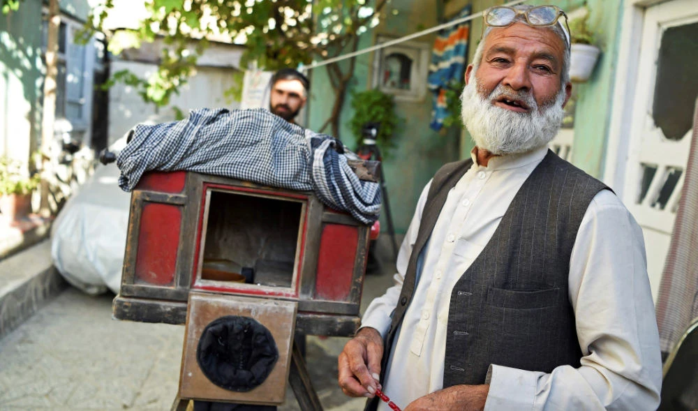 In this photo taken on October 13, 2021, Afghan photographer Haji Mirzaman (R) stands next to his homemade wooden box camera. (AFP)