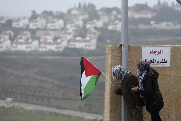 Protesters fly the Palestinian flag against the backdrop of the Israeli settlement of Halamish. (Reuters)