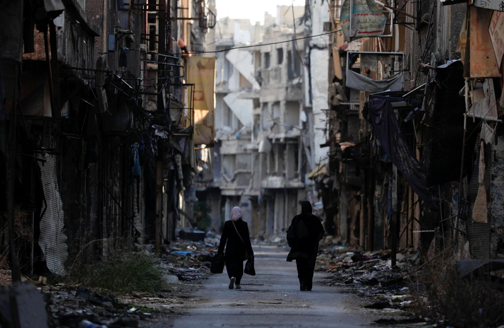 Women walk past damaged buildings in the Yarmouk Palestinian refugee camp on the southern outskirts of Damascus, Syria, Dec. 1, 2020. (Reuters)