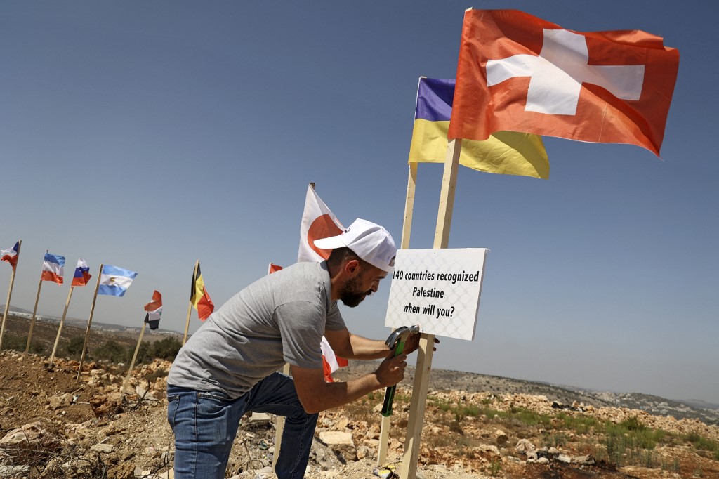Above, a Palestinian activist attaches a sign to the Swiss flag at the newly erected camp dubbed the United Nations camp near the Israeli settlement of Ariel in West Bank. (AFP)