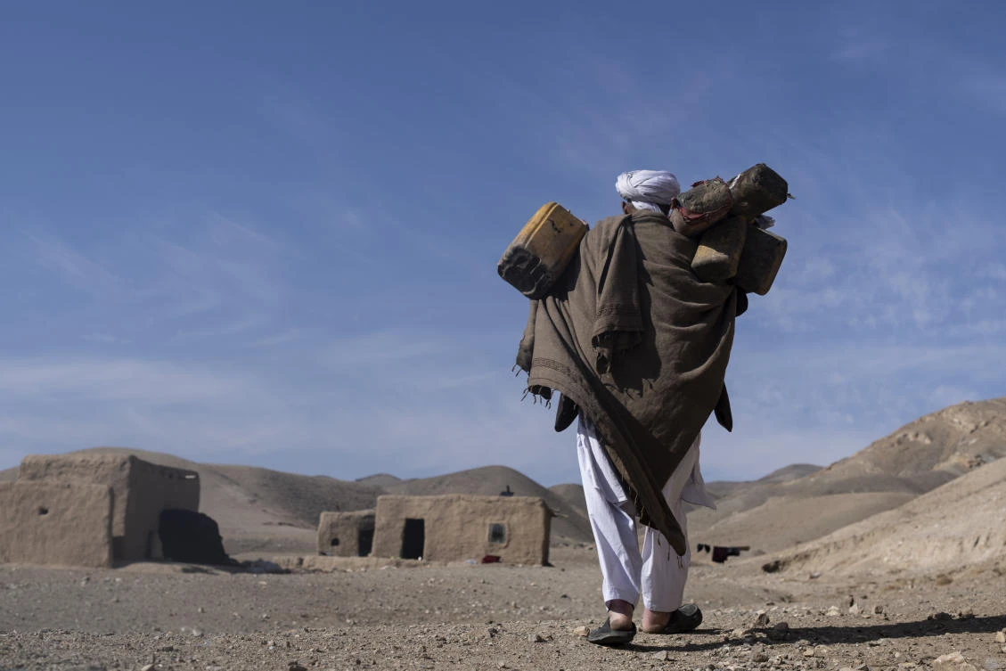 Hajji Wali Jan, 66, carries plastic containers for water on his way to his house in Kamar Kalagh village outside Herat, Afghanistan, Friday, Nov. 26, 2021. (AP)