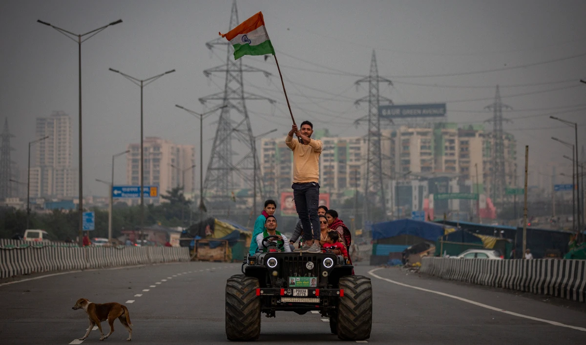 A farmer waves an Indian flag as he stands on the bonnet of a vehicle at a major expressway in Ghazipur, outskirts of New Delhi, India, Thursday, Dec. 9, 2021. (AP)
