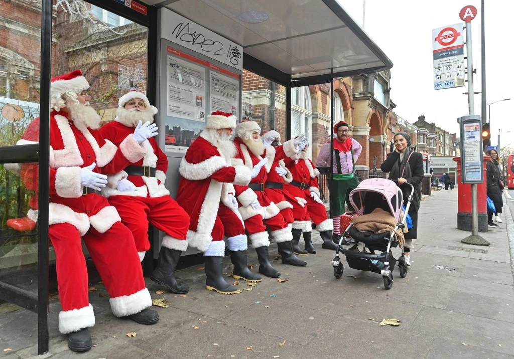 Santas wait at a bus stop as they take a break from the classroom during Santa School at The Ministry of Fun in London on Nove. 30, 2021. (AFP)