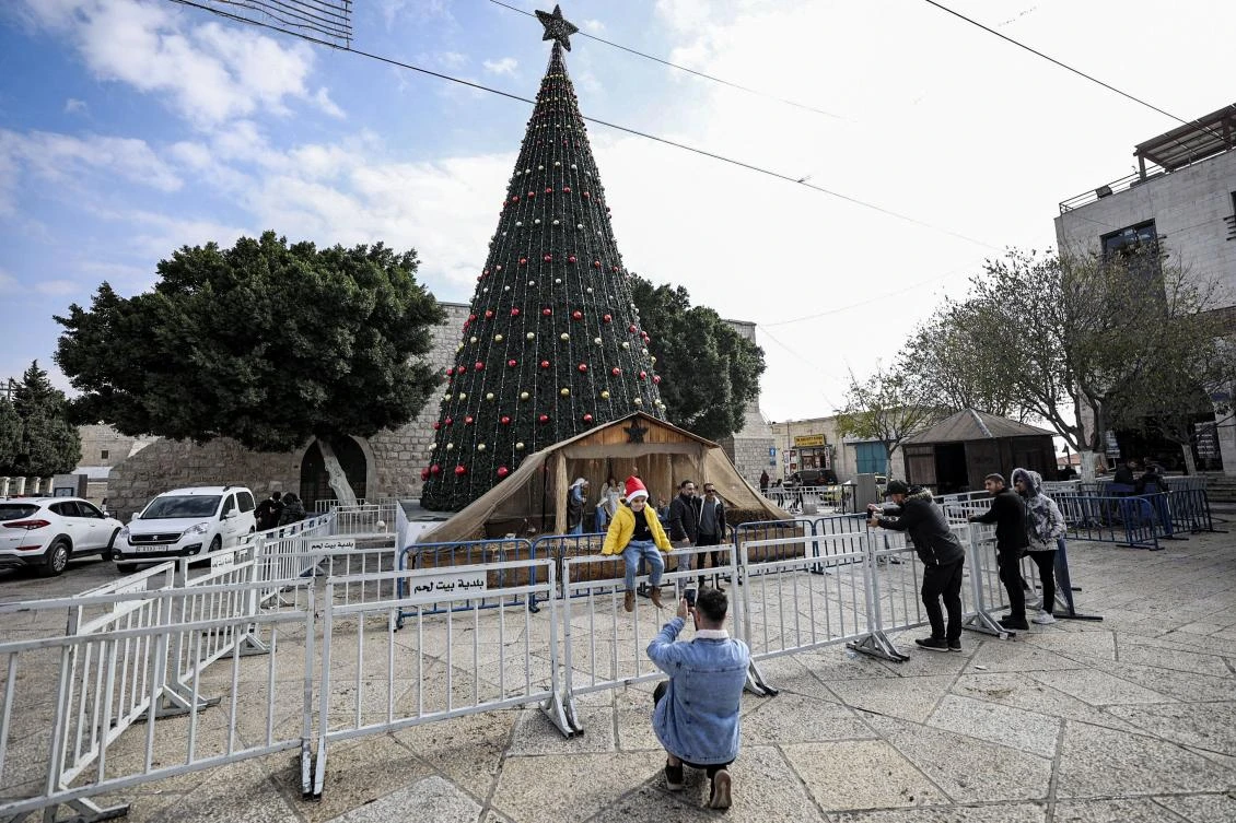 A child poses for a picture before the giant Christmas tree in the almost empty Manger Square outside the Church of the Nativity, in the biblical West Bank city of Bethlehem on December 15, 2021. (AFP)