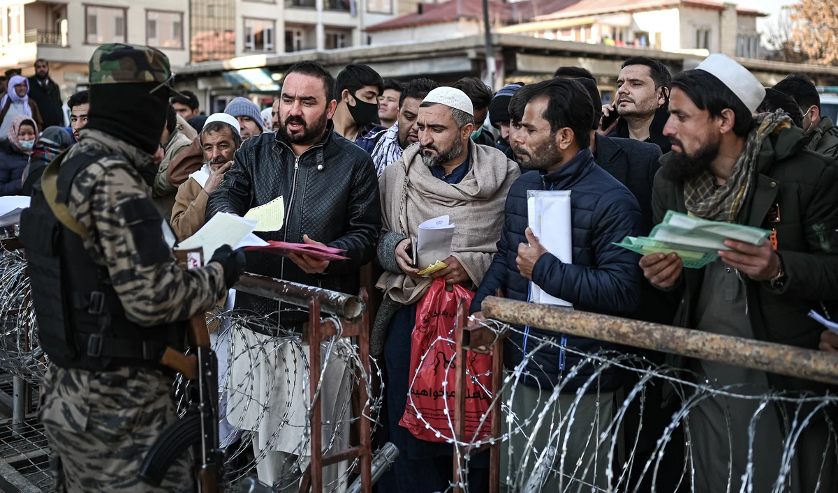 A Taliban fighter inspects documents of people queuing to enter the passport office in Kabul, Afghanistan, on December 18, 2021. (AFP)
