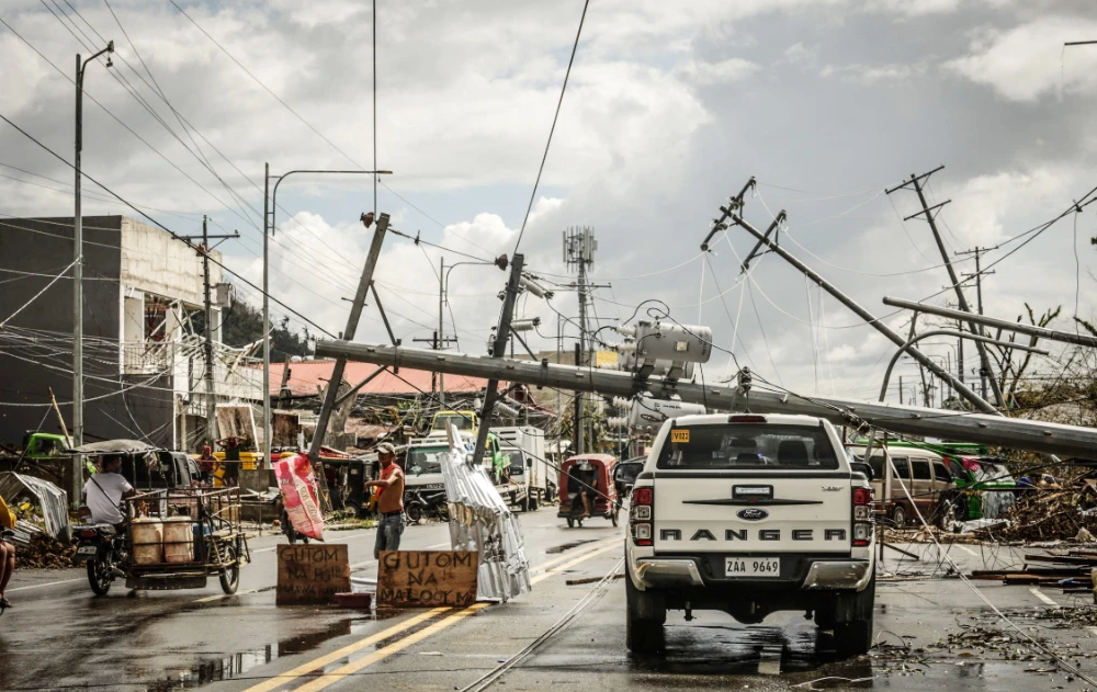 Fallen electric pylons block a road while a sign asking for food (L) is displayed along a road in Surigao City, Surigao del norte province, on December 19, 2021, days after super Typhoon Rai devastated the city. (AFP)
