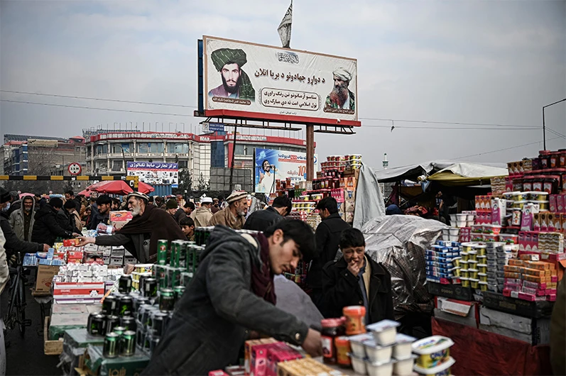 People shop as a billboard displaying the Taliban founder and late supreme leader Mullah Omar (L) and late leader of the Haqqani militant network Jalaluddin Haqqani (R) is seen at a market in Kabul on December 26, 2021. (AFP)