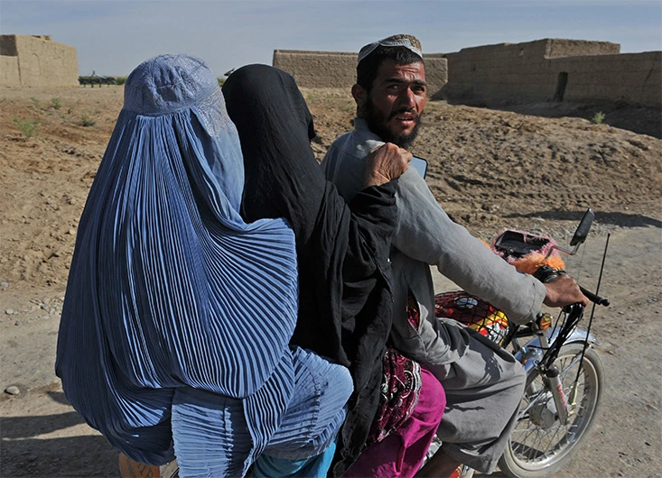 An Afghan man and two burqa clad women ride a motorcycle past in Khanashin District, Helman province, on April 24, 2011. (AFP/ FILE)