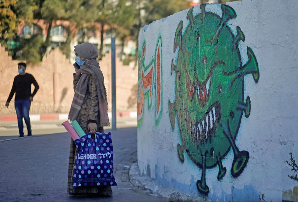 A Palestinian woman wearing on a protective face mask speaks on her phone as she stands next to a coronavirus-themed mural amid the coronavirus disease outbreak in Gaza on November 22, 2020. (REUTERS/File)