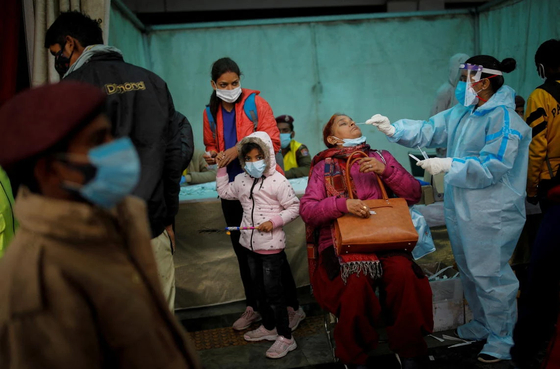 A healthcare worker collects a coronavirus disease (COVID-19) test swab sample from a woman amidst the spread of the disease, at a railway station in New Delhi, India, January 5, 2022. (Reuters)