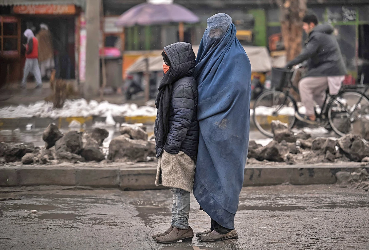 A burqa-clad Afghan woman stands with a child as she seeks alms from people passing by along a road in Kabul, Afghanistan, on January 8, 2022. (AFP)