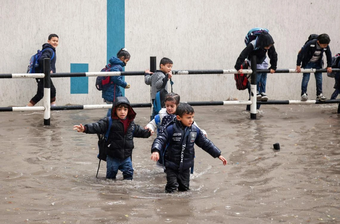 Palestinian UNRWA school pupils cross a flooded street in the heavy rain in Gaza City, on January 15, 2022. (AFP)