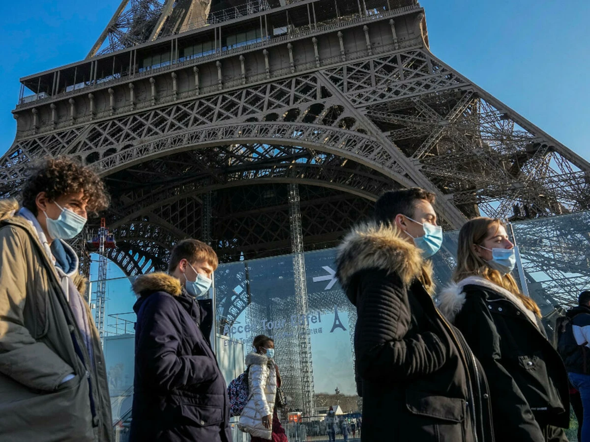 People wearing face masks to protect against Covid-19 walk past the Eiffel Tower in Paris, on December 21, 2021 (AP)