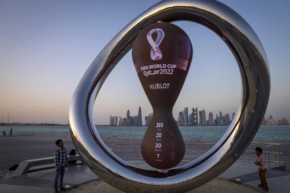 Children stand next to the official countdown clock showing remaining time until the kick-off of the World Cup 2022, in Doha, Qatar, Nov. 25, 2021. Fans can start registering for the lottery to buy Qatar World Cup tickets Wednesday, Jan. 19, 2022. (AP)