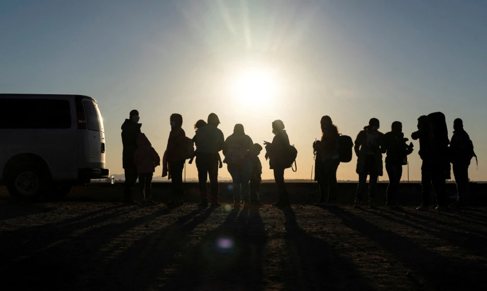 Migrants seeking asylum in the US, mostly from Venezuela, stand near the border fence while waiting to be processed by the US border patrol after crossing the border from Mexico at Yuma, Arizona, US. (Reuters)