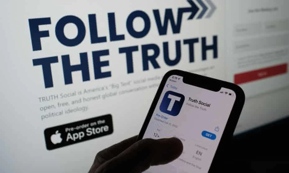 A person checking the app store on a smartphone for "Truth Social", with it's website on a computer screen in the backgrounD. (AFP)