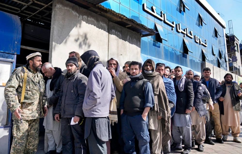 A Taliban fighter stands guard in front of people waiting to enter a bank, in Kabul, Afghanistan, Sunday, Feb. 13, 2022. (AP)