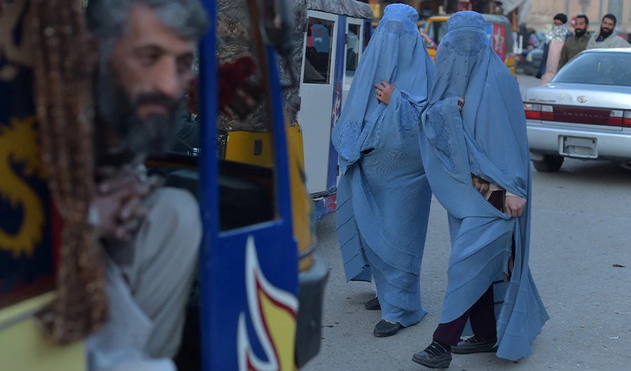 A rickshaw taxi driver looks on as burqa clad- women walk a long road, in Herat on February 15, 2022. (AFP)