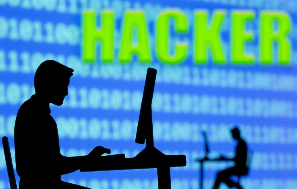 A 3D printed model of men working on computers are seen in front of displayed binary code and words "Hacker" in this illustration taken, July 5, 2021. (REUTERS)