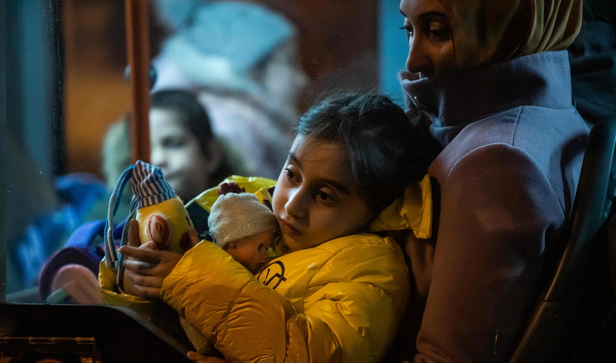 A young refugee coming from Ukraine sit on a woman's lap inside a bus after arriving at the North Railway Station in Bucharest, early March 4, 2022. (AFP)