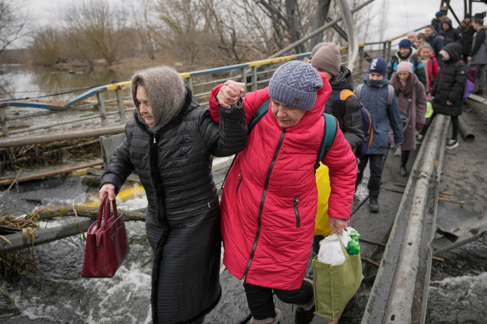 Women hold hands while crossing the Irpin river on an improvised path under a bridge that was destroyed by a Russian airstrike, while assisting people fleeing the town of Irpin, Ukraine, Saturday, March 5, 2022. (AP)