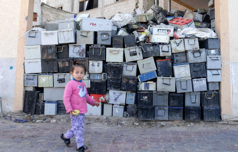 A Palestinian girl walks past a stack of discarded batteries slated for recycling in Khan Yunis in the southern Gaza Strip, on February 14, 2022. (AFP)