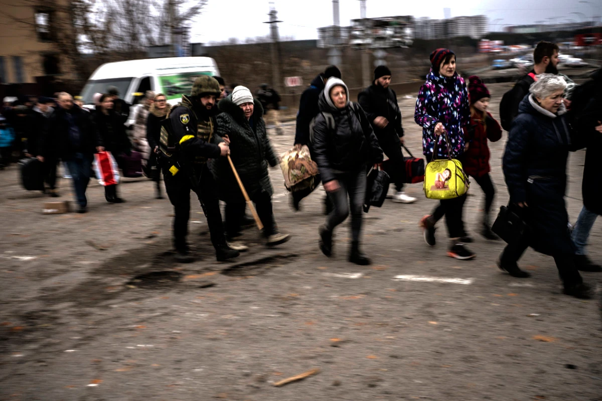 A Ukrainian police officer helps people as artillery echoes nearby while fleeing Irpin in the outskirts of Kyiv on March 7, 2022. (AP Photo/Emilio Morenatti)