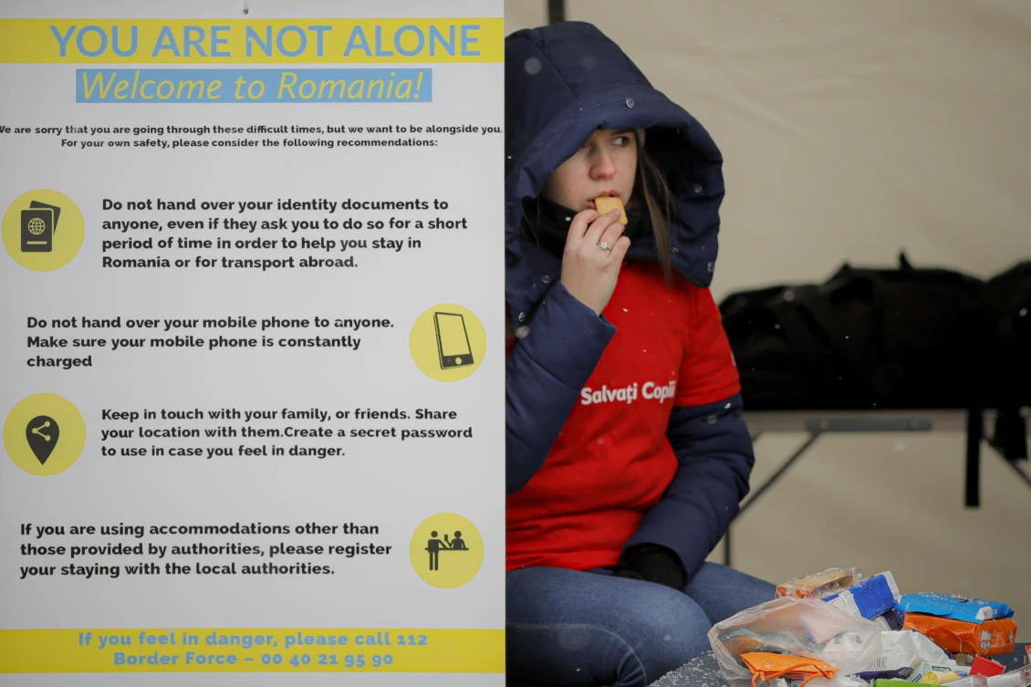 A volunteer at the international humanitarian group Save the Children sits next to a banner giving advice on personal safety at the Romanian-Ukrainian border, in Siret, Romania, Monday, March 7, 2022. (AP)