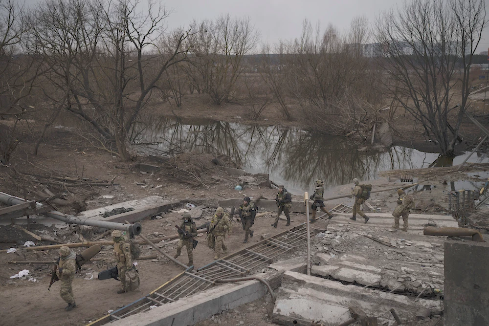 Ukraine’s military and volunteer forces are preparing for an all-out assault on the capital. Above, soldiers cross an improvised path under a destroyed bridge in the outskirts of Kyiv on Mar. 12, 2022. (AP)