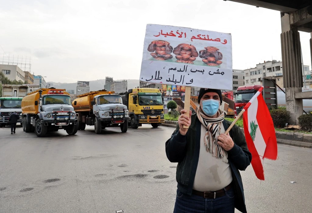 A Lebanese protester holds a sign as fuel tankers block a road in Lebanon's capital Beirut during a general strike by public transport and workers unions.(AFP)