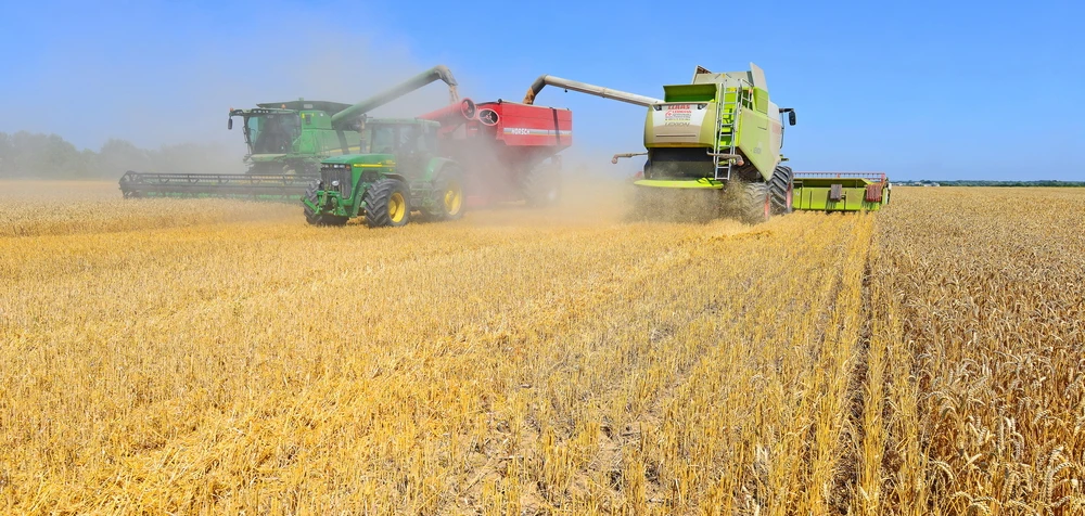 Modern John Deere tractor with a tank for transportation of grain near the combines harvesting. in the field near the town Kalush, Western Ukraine. Shutterstock