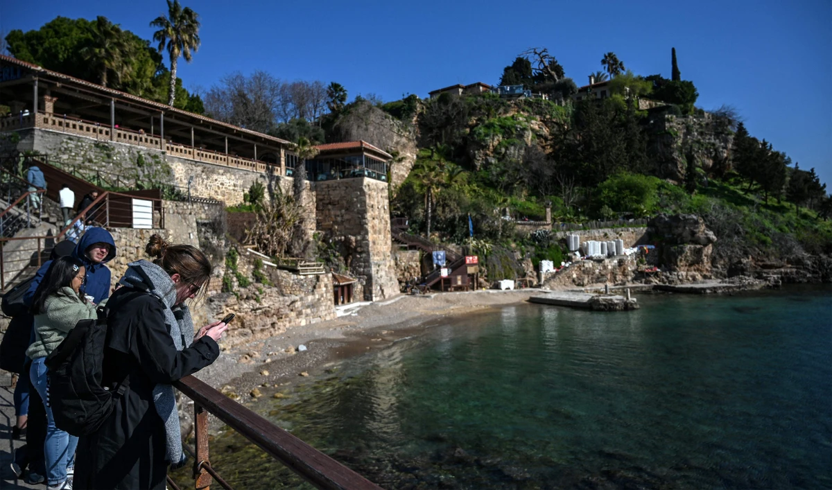 Tourists stand near the beach at Kaleici marina on March 12, 2022 in Antalya. (AFP)