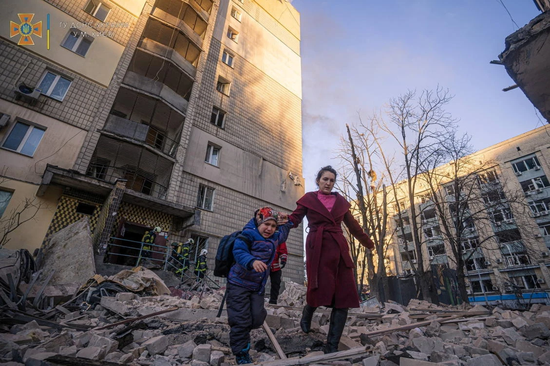 A woman with a child evacuates from a residential building damaged by shelling in Kyiv, Ukraine. (State Emergency Service of Ukraine via Reuters)