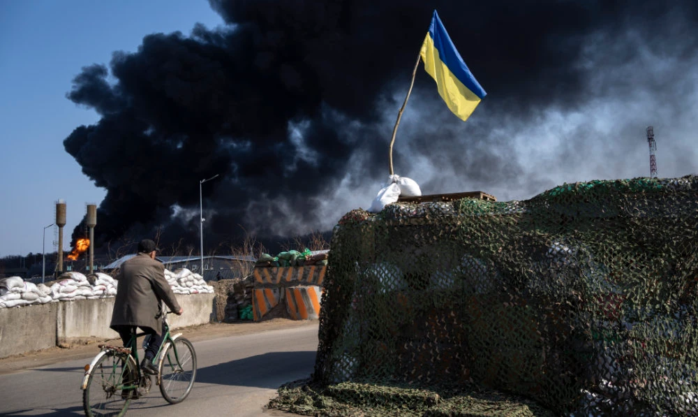 A man rides a bicycle as black smoke rises from a fuel storage of the Ukrainian army following a Russian attack, on the outskirts of Kyiv, Ukraine, Friday, March 25, 2022. (AP)