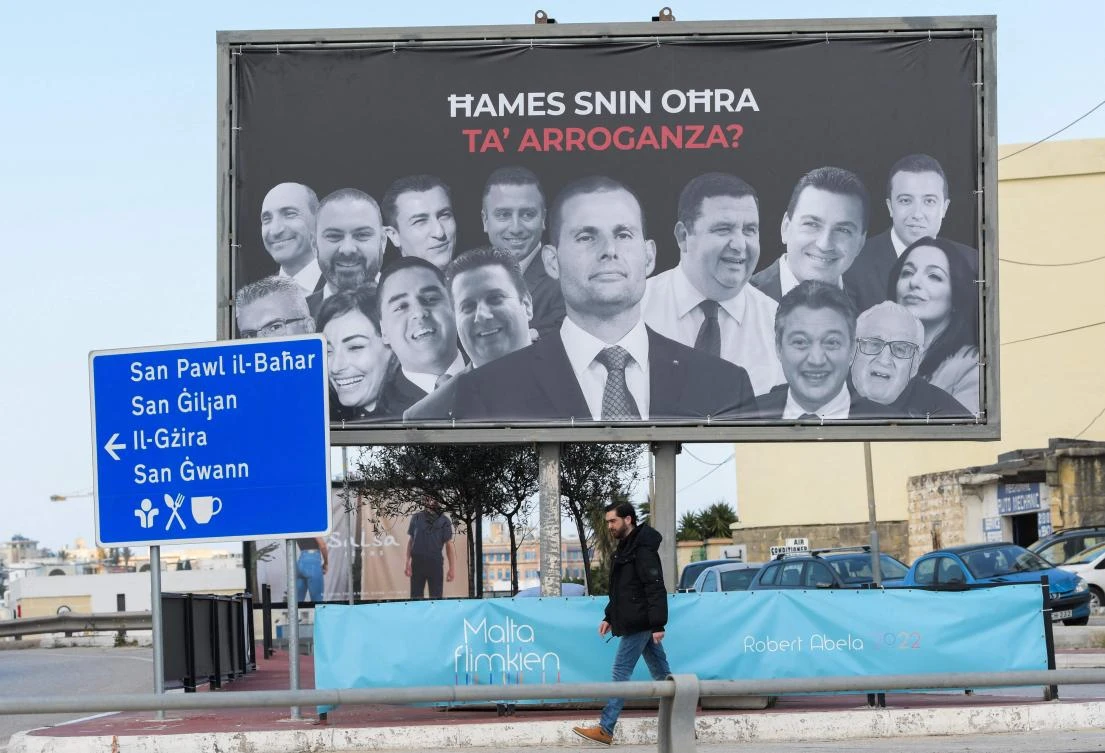 A man walks past an opposition election billboard in Msida, Malta, featuring Labour Party prime minister Robert Abela, center, and members of parliament, reading ‘Five more years of arrogance’. (AFP)
