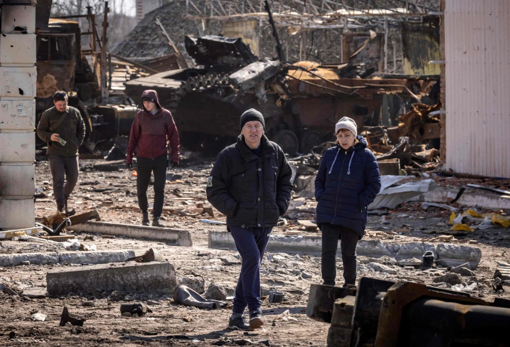 Residents walk amid rubble near a destroyed Russian tank in the northeastern city of Trostianets, on March 29, 2022. (AFP)