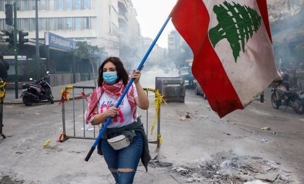 A demonstrator carries the national flag during a protest against the fall in the Lebanese pound and mounting economic hardships, Beirut, Lebanon, Mar. 16, 2021. (Reuters)