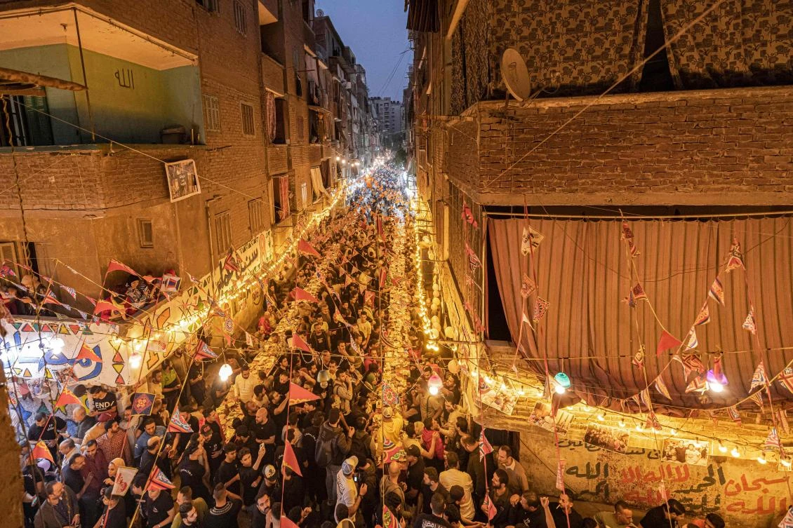 Muslims gather along a street-long table for break their Ramadan fast together in a mass "iftar" meal on the 15th day of the Muslim holy month, in the Matariya suburb in the northeast of Egypt's capital Cairo on April 16, 2022. (AFP)