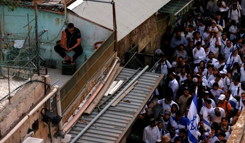 A Palestinian man sits on a roof, above an alley, as Israelis march inside Jerusalem’s Old City, May 29, 2022. (Reuters)