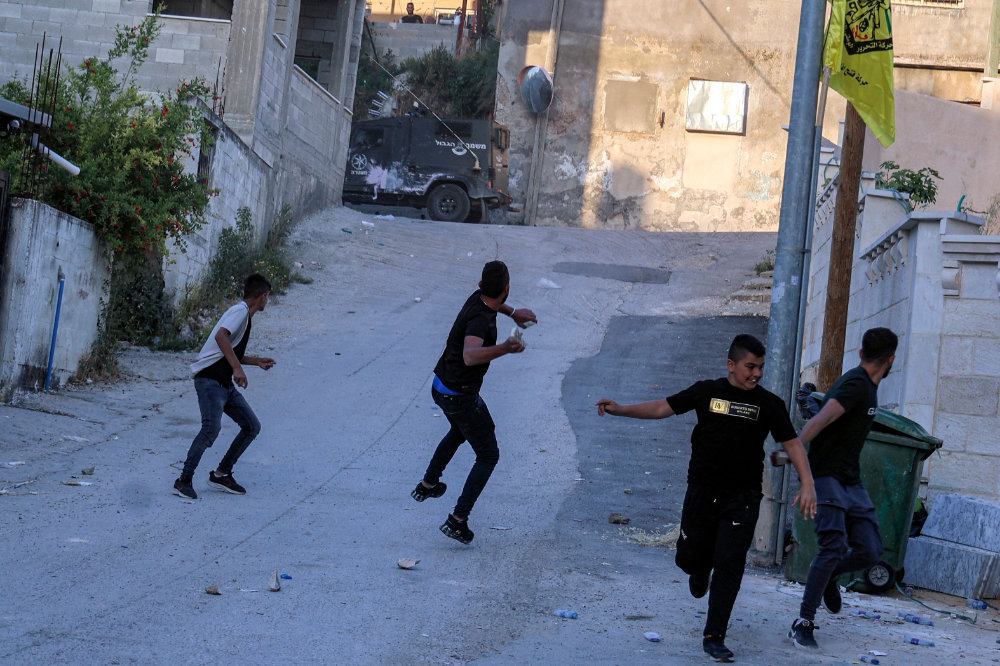 Palestinian youths throw stones at Israeli forces' vehicles during their a raid on a house in the occupied West Bank. (AFP)
