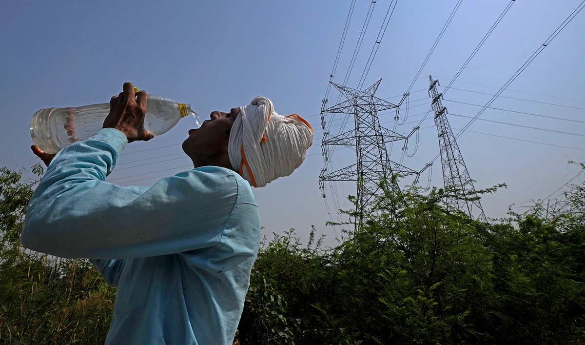 A workers quenches his thirst next to power lines as a heatwave continues to lashes the capital, in New Delhi, India, Monday, May 2, 2022. (AP)