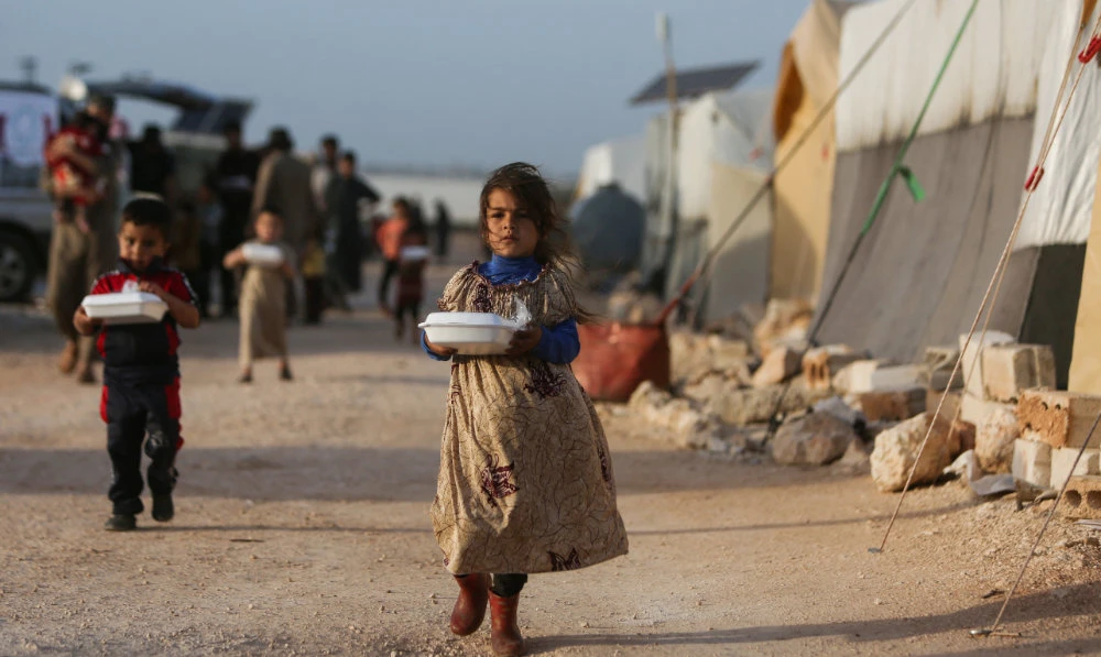 Displaced Syrian children return to their tents with boxes of food distributed by a local charity organization at a camp for displaced people in Idlib province. (AFP)