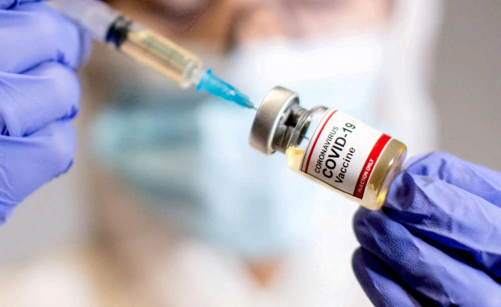 A woman holds a small bottle labelled with a "Coronavirus COVID-19 Vaccine" sticker and a medical syringe in this illustration taken October 30, 2020. (REUTERS)
