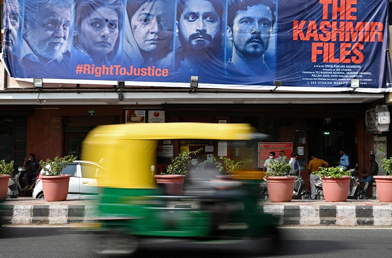 An auto rickshaw moves past a banner of Bollywood movie 'The Kashmir Files' installed outside a cinema hall in the old quarters of Delhi on March 21, 2022. (AFP)