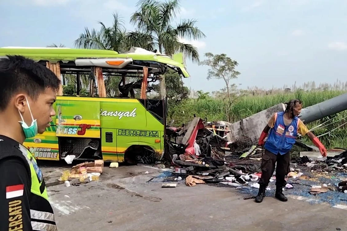 Rescuers inspect the wreckage of a tourist bus that crashed into a street sign on a highway in Mojokerto, East Java on May 16, 2022. (AP)