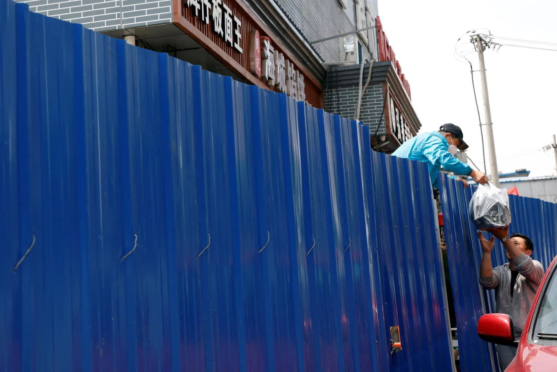 A worker in protective suit receives supply through the fence of a barricaded residential area under lockdown in Beijing, China on May 17, 2022. (Reuters)