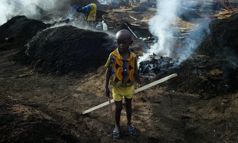 A child stands in a Côte d’Ivoire charcoal yard, while his mother works. (UNICEF)