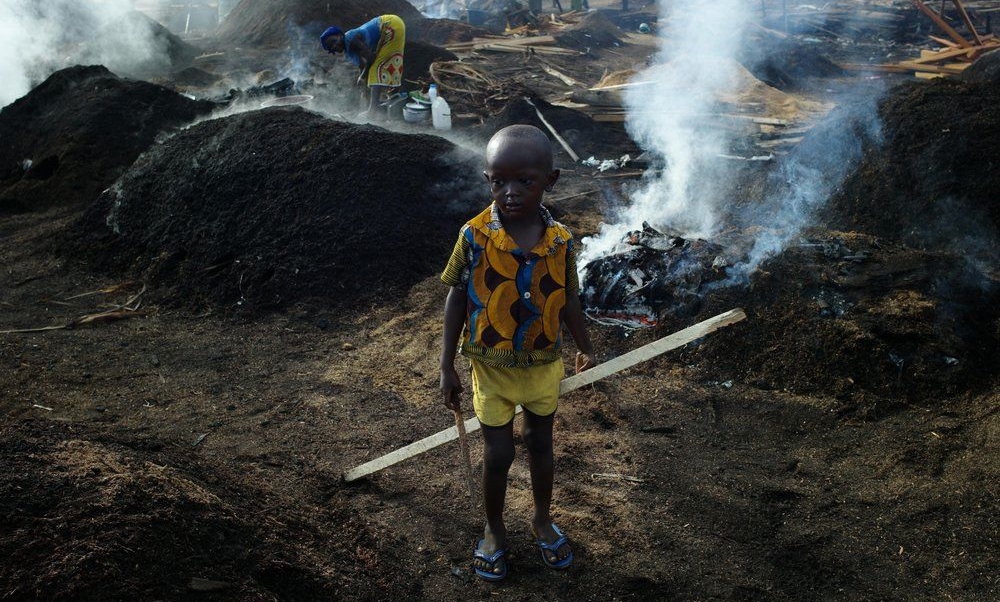 A child stands in a Côte d’Ivoire charcoal yard, while his mother works. (UNICEF)
