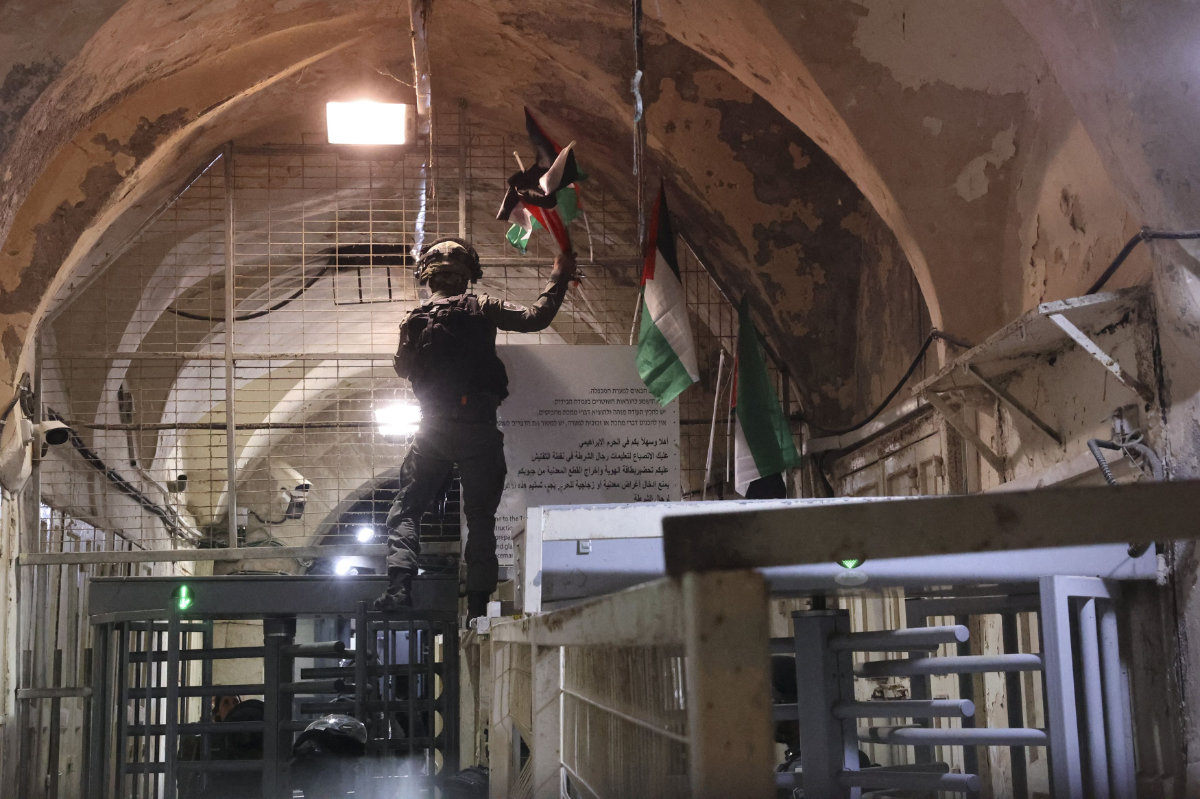 An Israeli soldier removes a Palestinian flag displayed by protesters at a market in Hebron on May 23, 2022. (AFP)