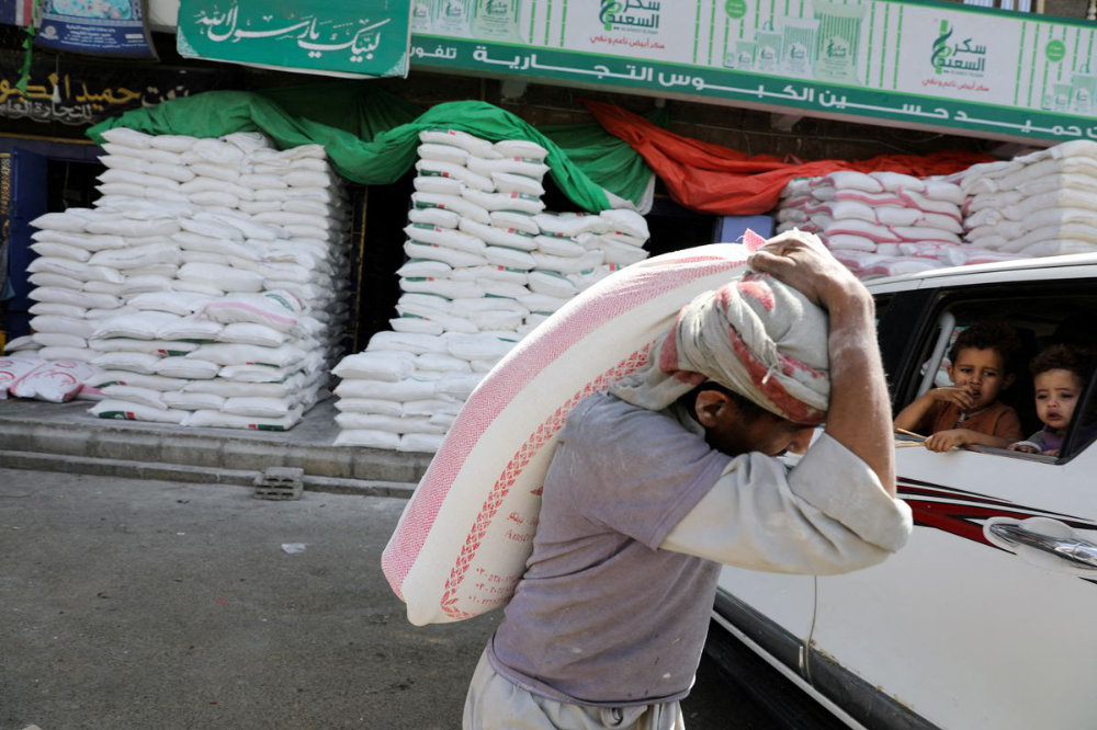 A worker carries a sack of wheat flour outside a wholesale food shop in Sanaa, Yemen. (Reuters)